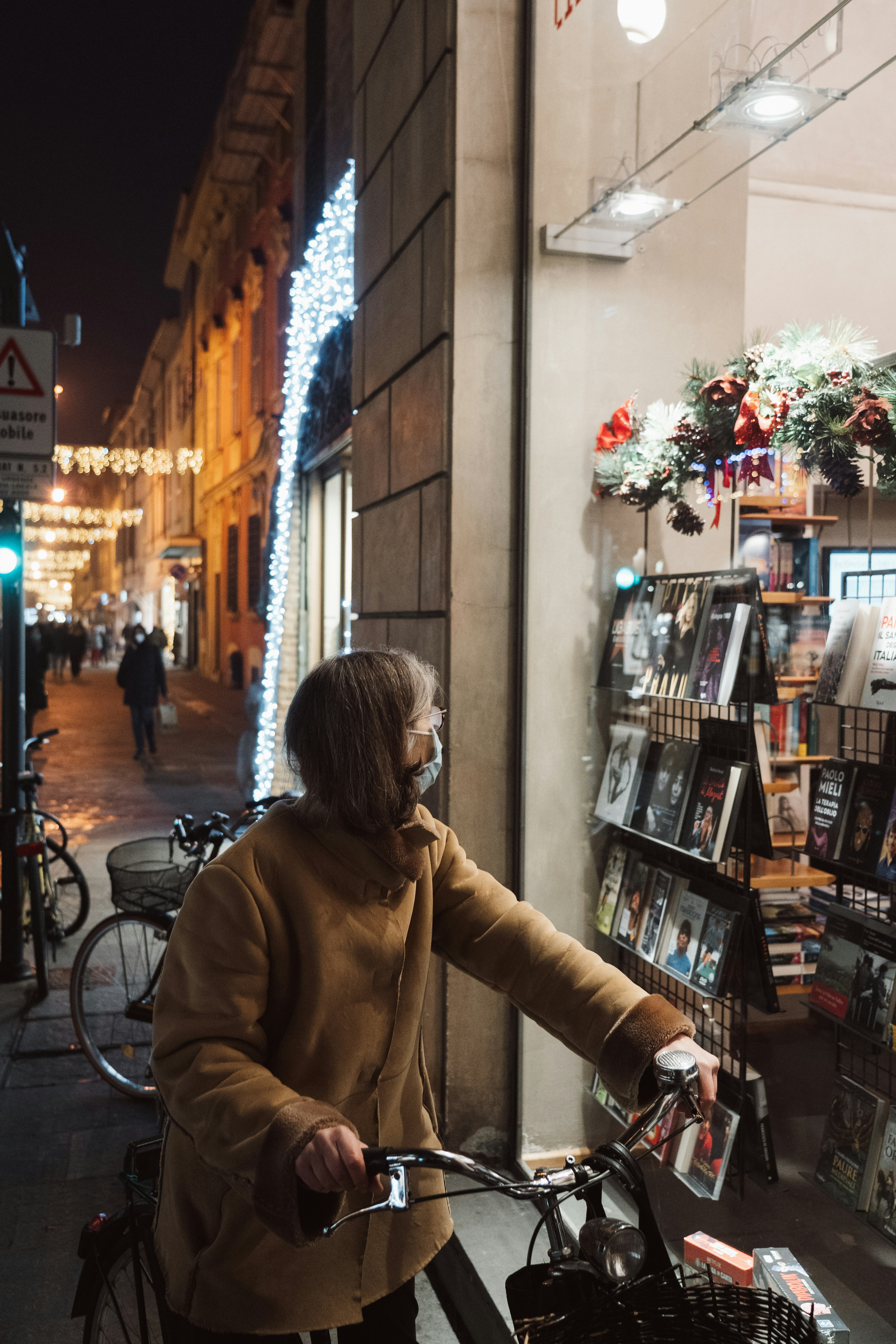 woman in brown coat standing in front of book shelf